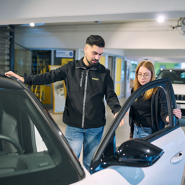 Verkäufer zeigt einer Kundin ein Auto im Autohaus