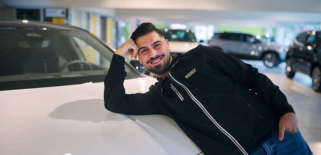 Verkäufer lehnt im Autohaus an der Motorhaube eines Autos
