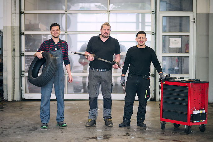 Werkstattmitarbeiter posieren mit verschiedenen Werkzeugen für ein Gruppenfoto in der Werkstatt