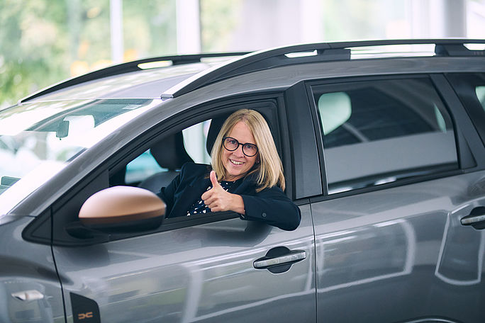 Geschäftsführerin lehnt aus dem Fahrerfenster und zeigt den Daumen nach oben