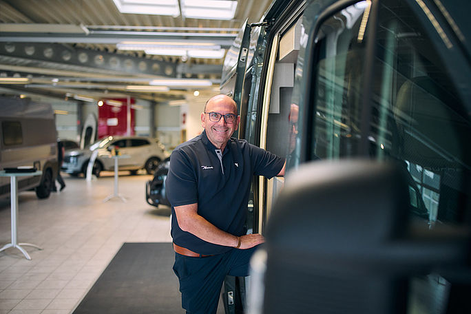 Verkäufer posiert neben einem Wohnwagen im Autohaus