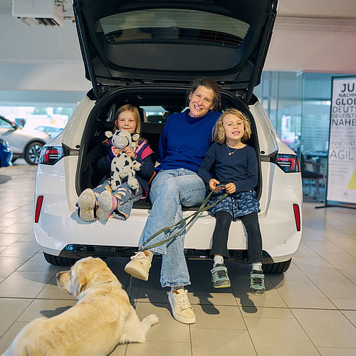 Geschäftsführerin mit zwei Kindern und einem Hund im Kofferraum sitzend