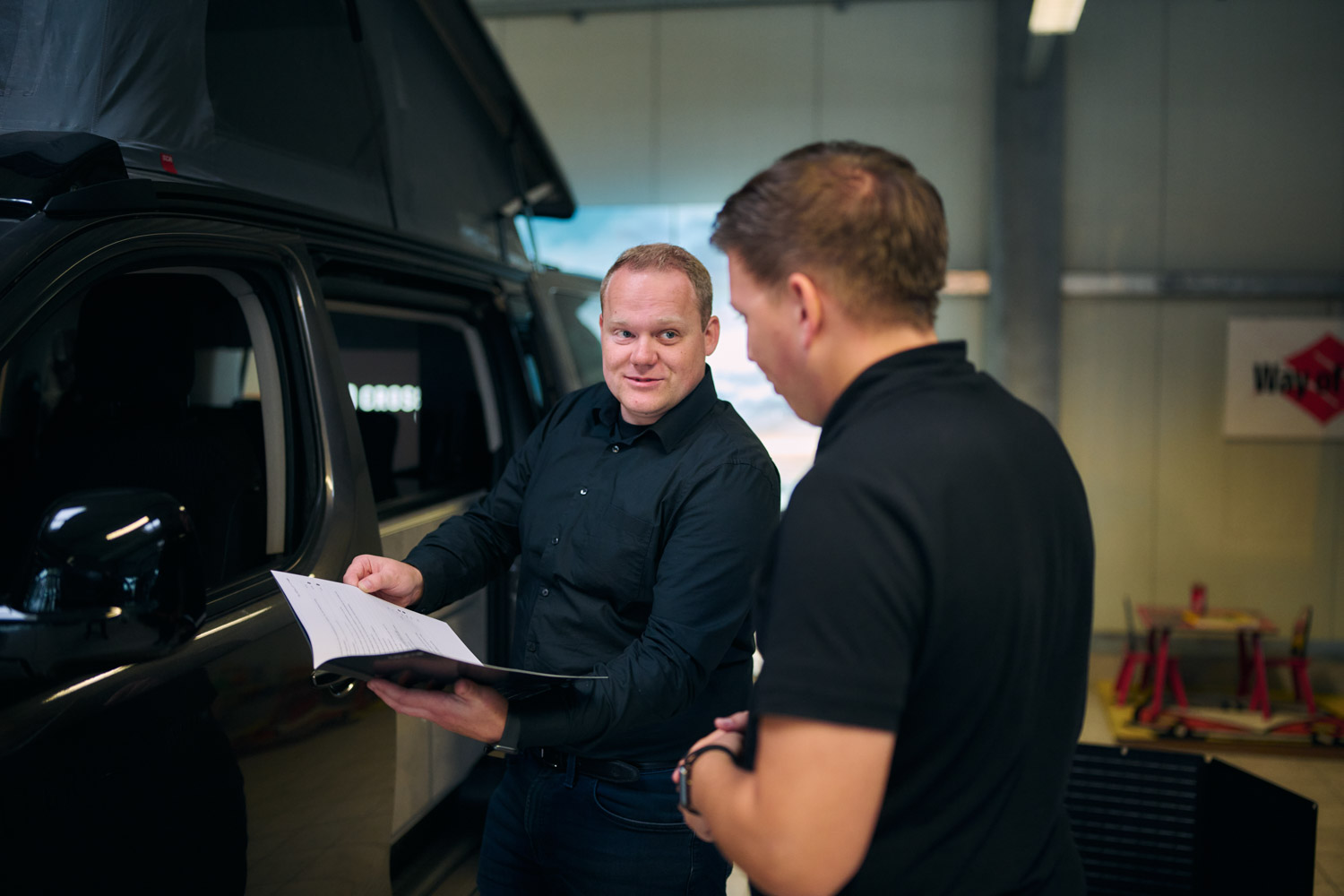 Verkäufer zeigt einem Kunden ein Prospekt bei einem Wohnmobil