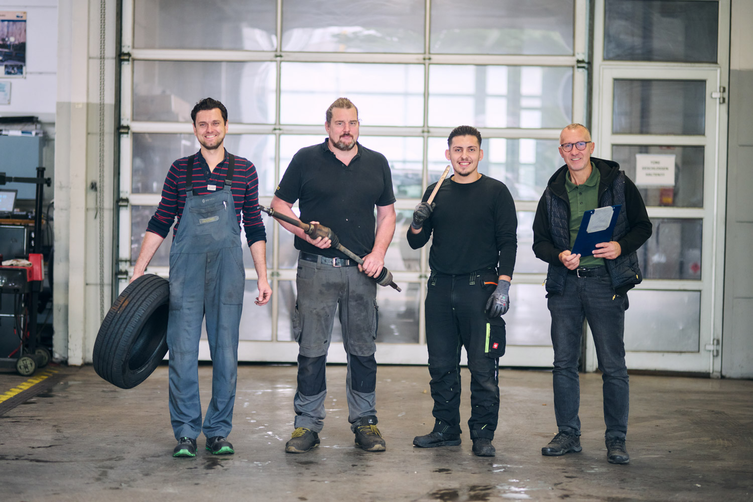 Werkstattmitarbeiter posieren mit verschiedenen Werkzeugen für ein Gruppenfoto in der Werkstatt